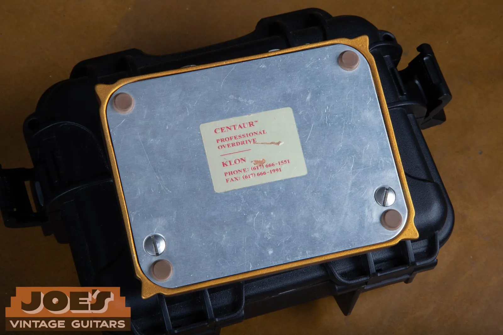 The aluminum bottom plate of a Klon Centaur showing brown rubber feet, slotted screws, and a cream label reading Centaur Professional Overdrive, Klon, with phone and fax numbers.