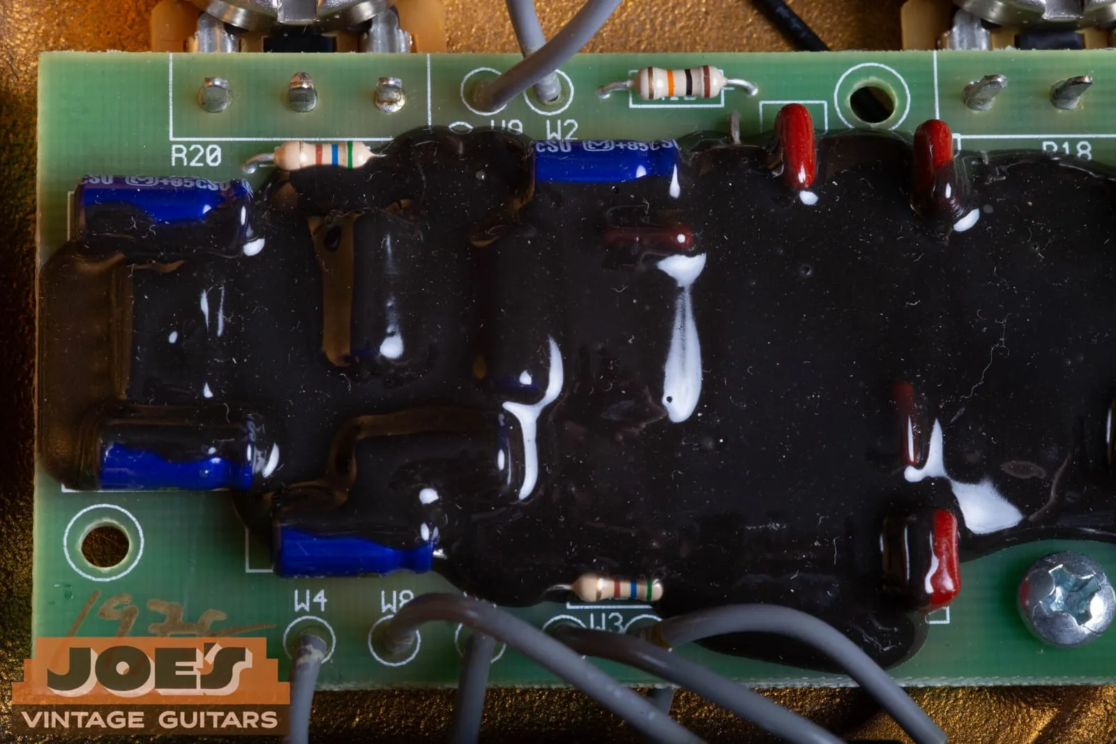 Overview of the green circuit board inside a Klon Centaur showing component silkscreen markings, blue capacitors, red resistors, grey wire loom, and the black epoxy.