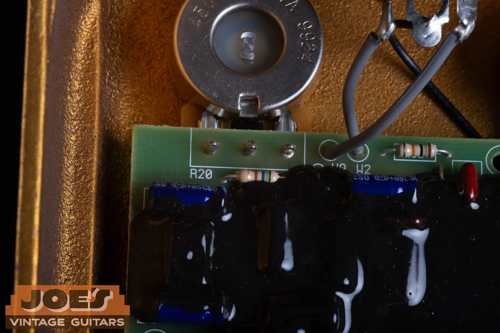 Interior of a gold Klon Centaur enclosure showing the rough textured cast surface, a CTS potentiometer, and the green circuit board with black epoxy.