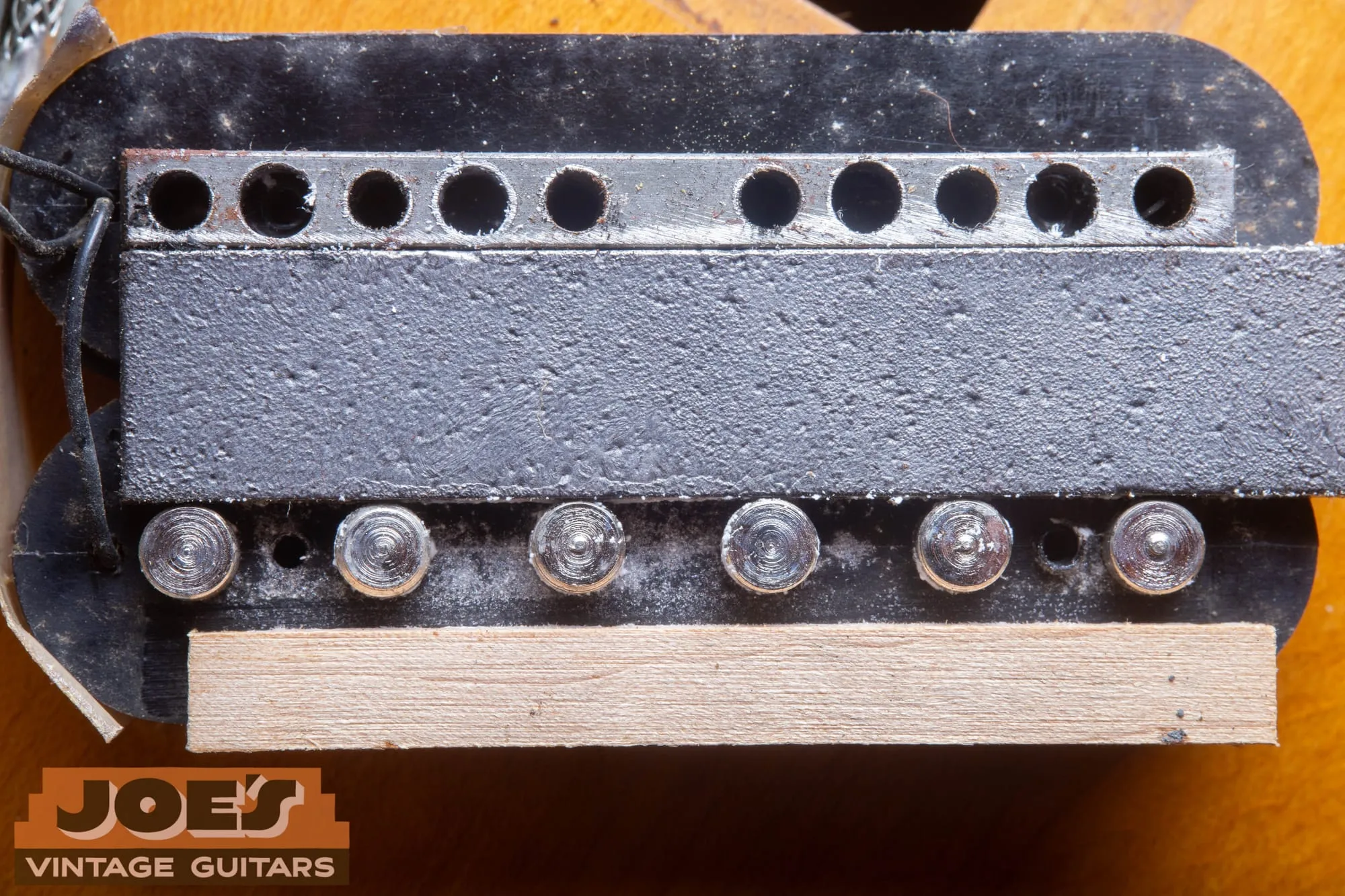 Inside of an opened Gibson PAF pickup showing the rough sand cast alnico bar magnet, steel keeper bar, pole screws, and maple wood spacer.