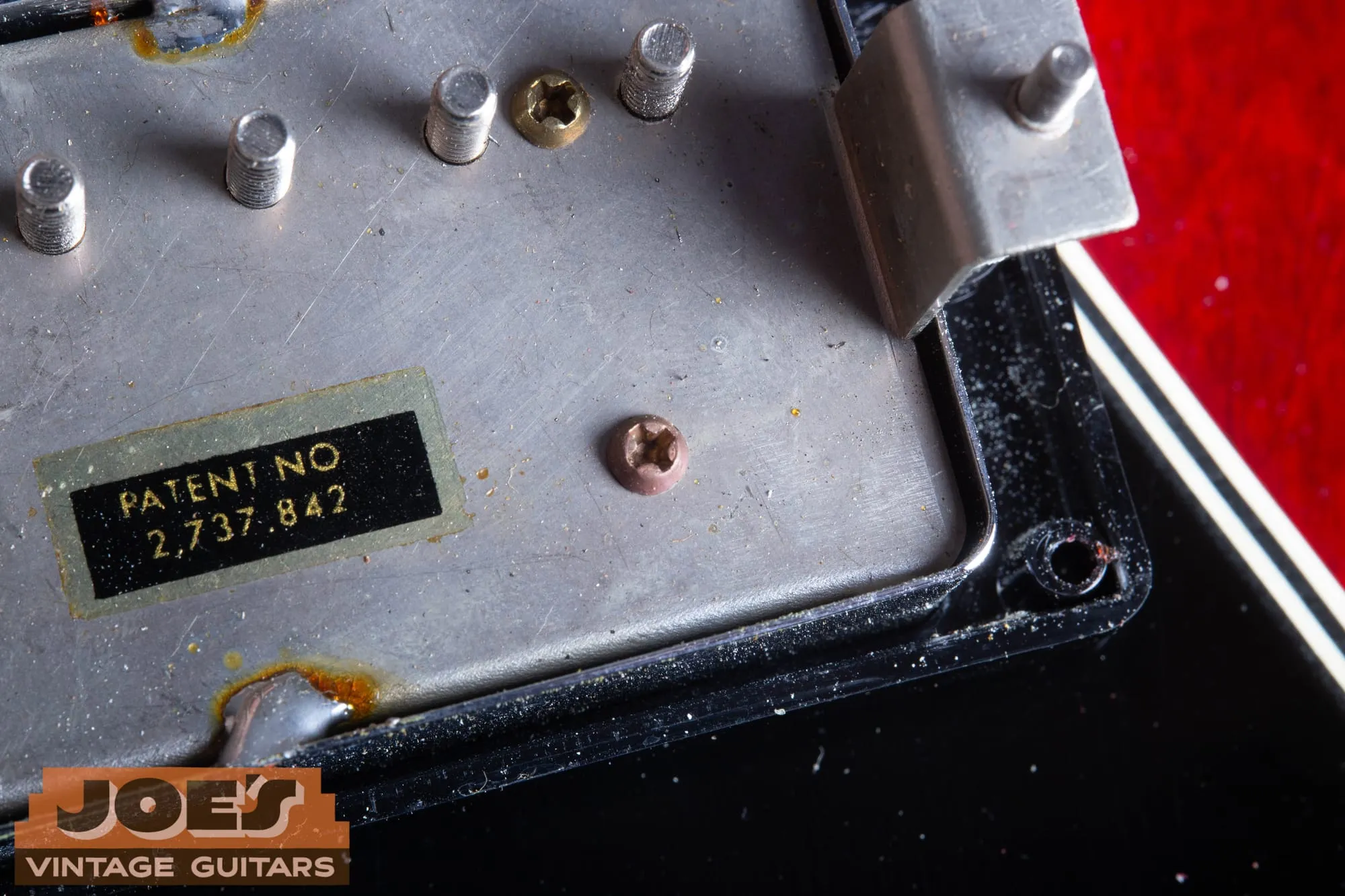 Underside of a patent number pickup showing the protruding pole screw ends, brass and copper toned Phillips bobbin screws, and the mounting leg.