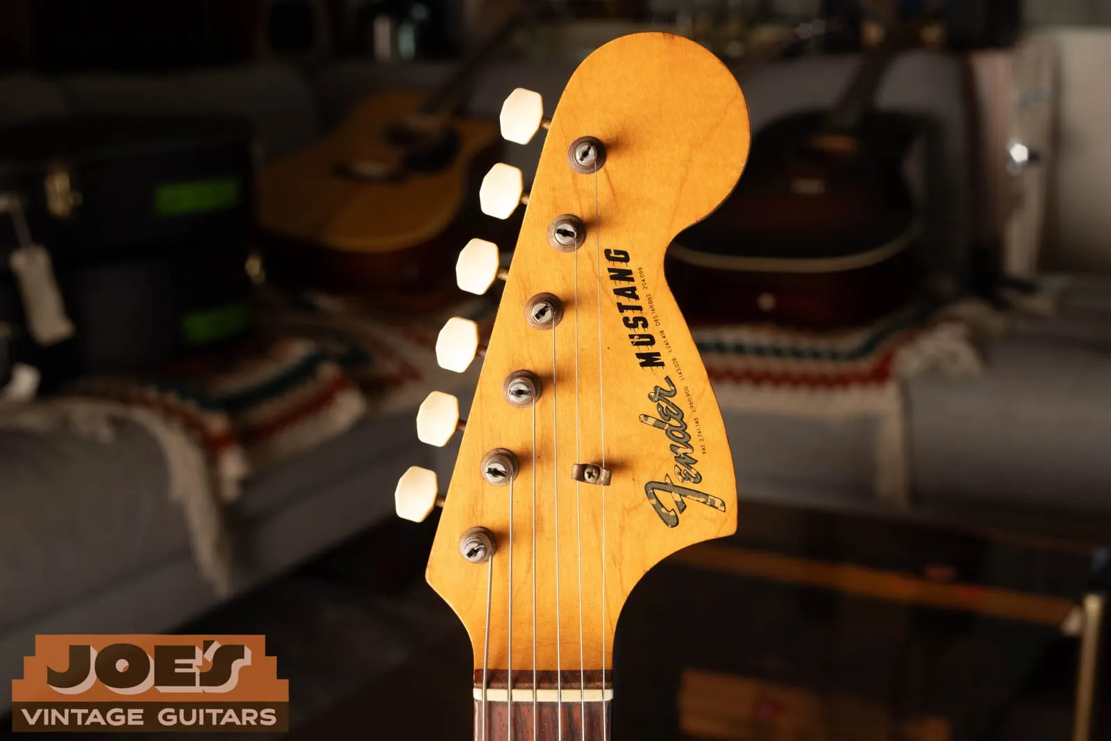 Headstock of a vintage Fender Mustang showing the gold transition Fender logo above the Mustang model name on a maple face.